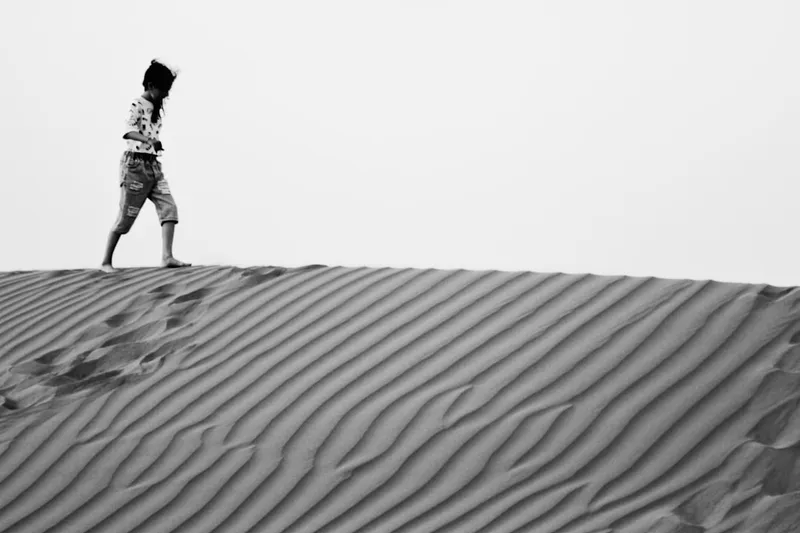 A person walks on top of a sand dune.