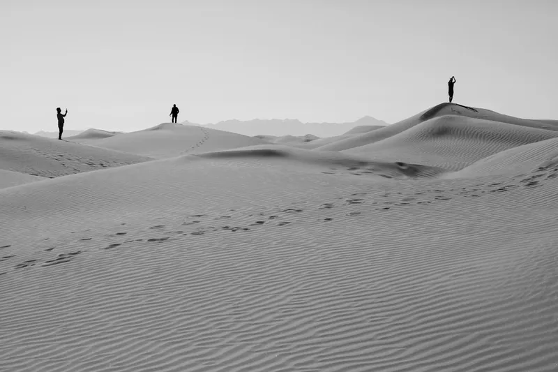 People stand atop desert sand dunes, reaching upwards.